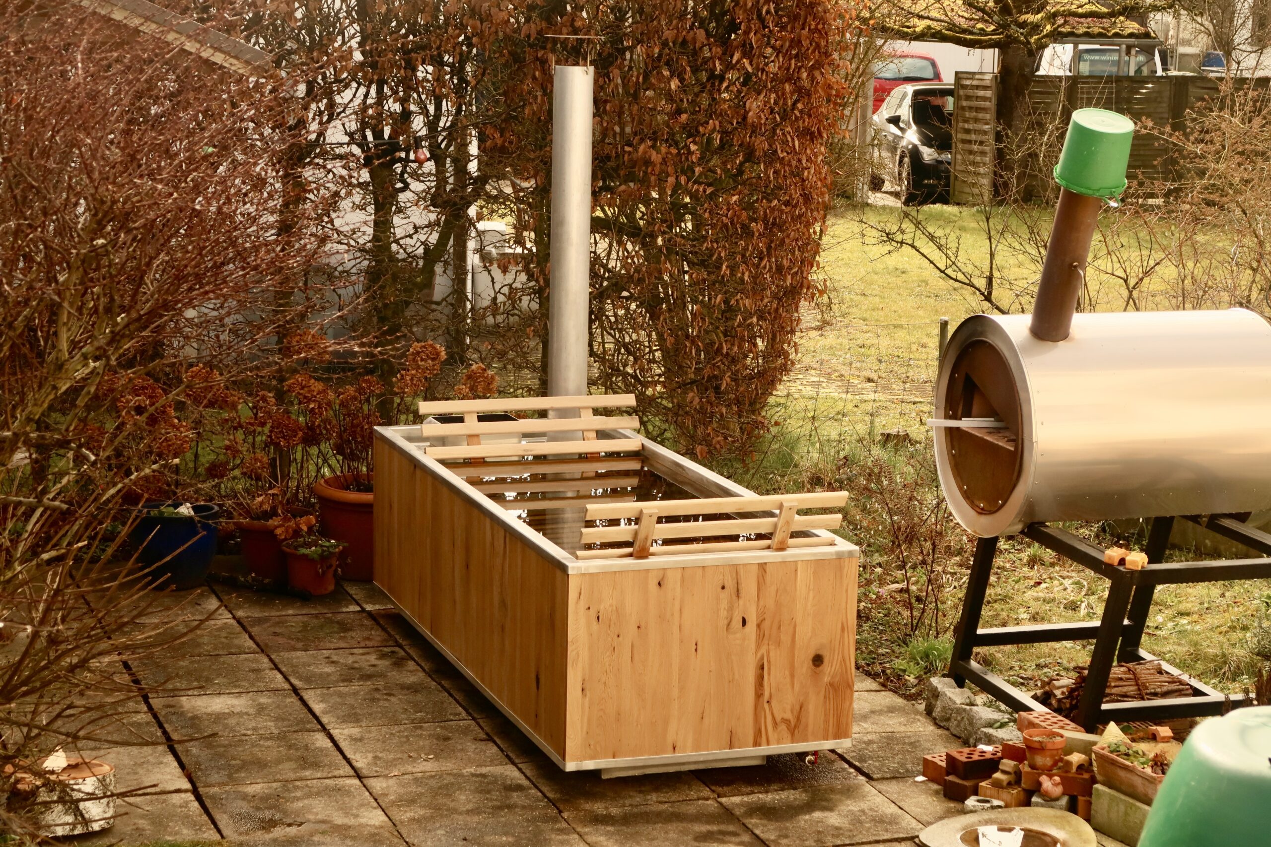 Hot Pot aus Holz mit Kamin für Feuerheizung auf einer Terasse mit Pflanzen